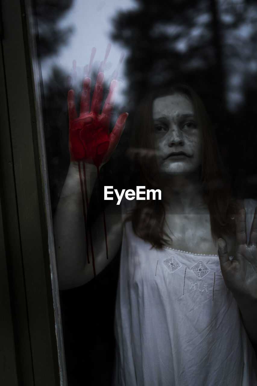Female ghost with blood on hand seen through window of haunted cabin