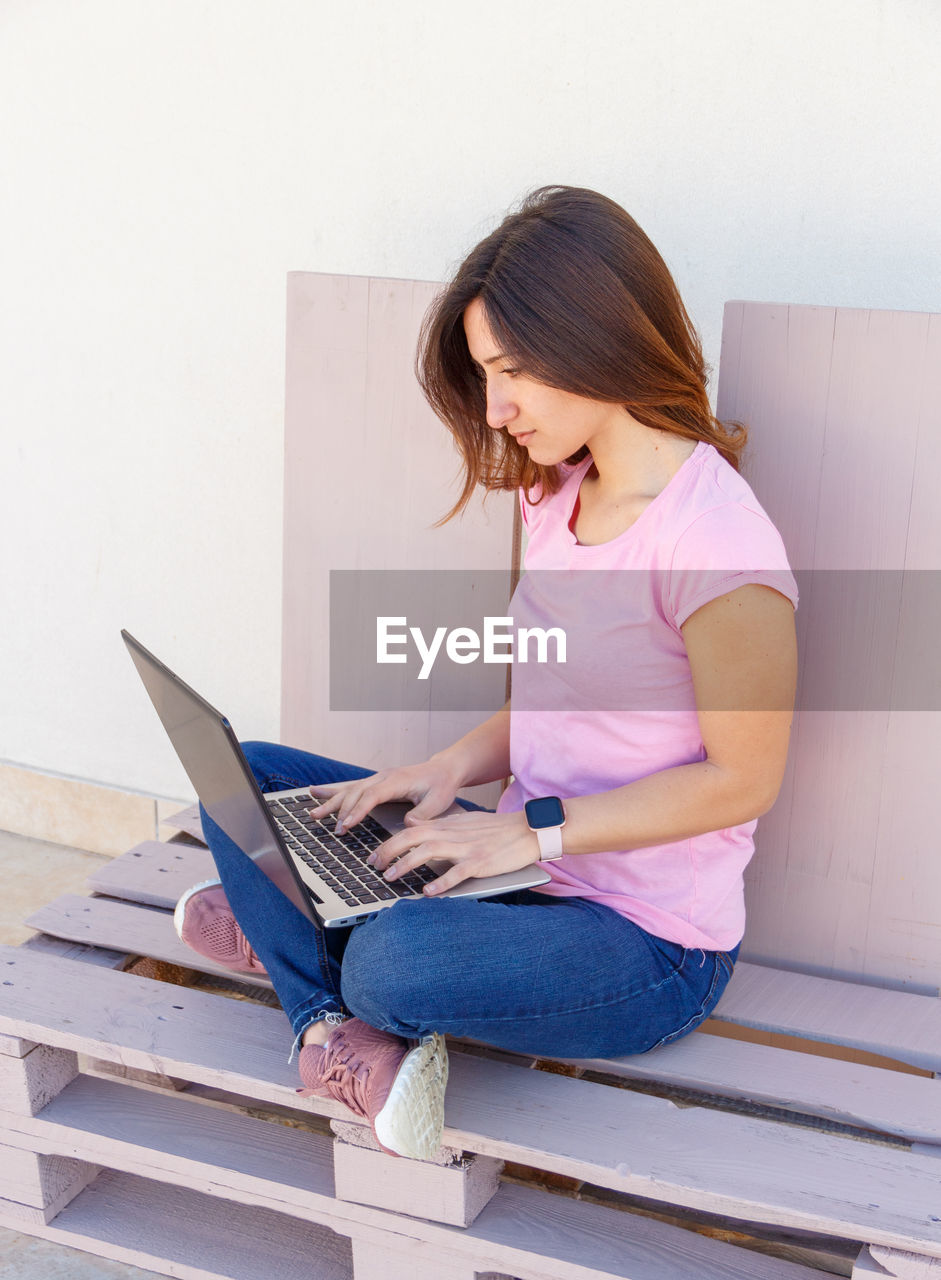 Young women wearing pink t-shirt and jeans using laptop outdoor