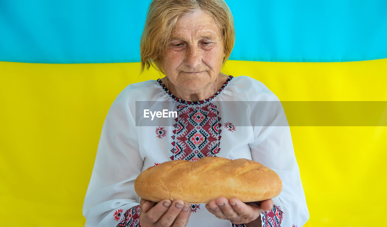 Senior woman holding bread against against ukrainian flag