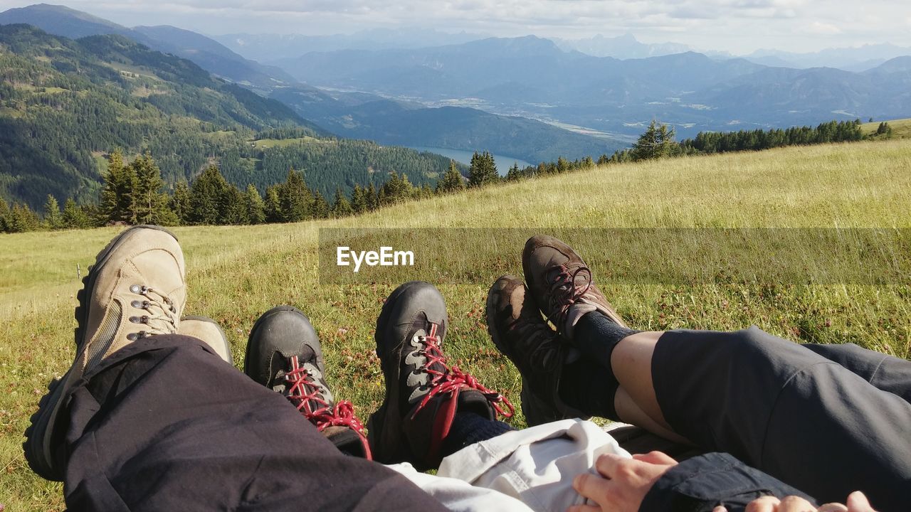 Low section of friends resting on grassy field at mountain