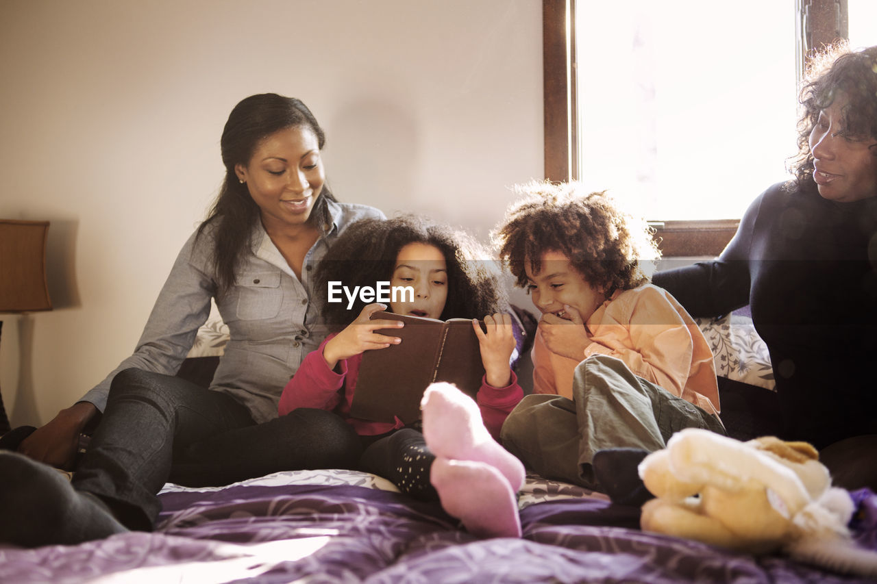 Happy family reading book while sitting on bed at home