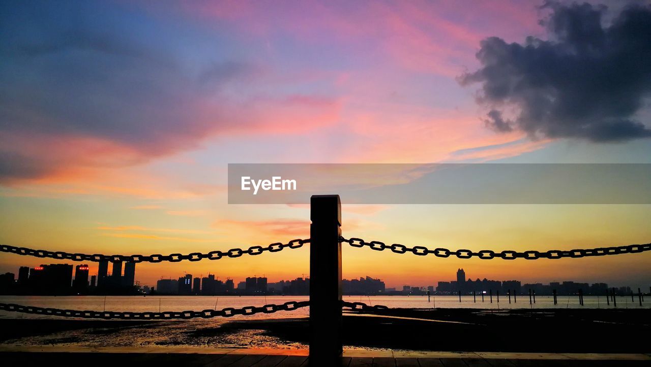 Silhouette bridge over sea against dramatic sky during sunset