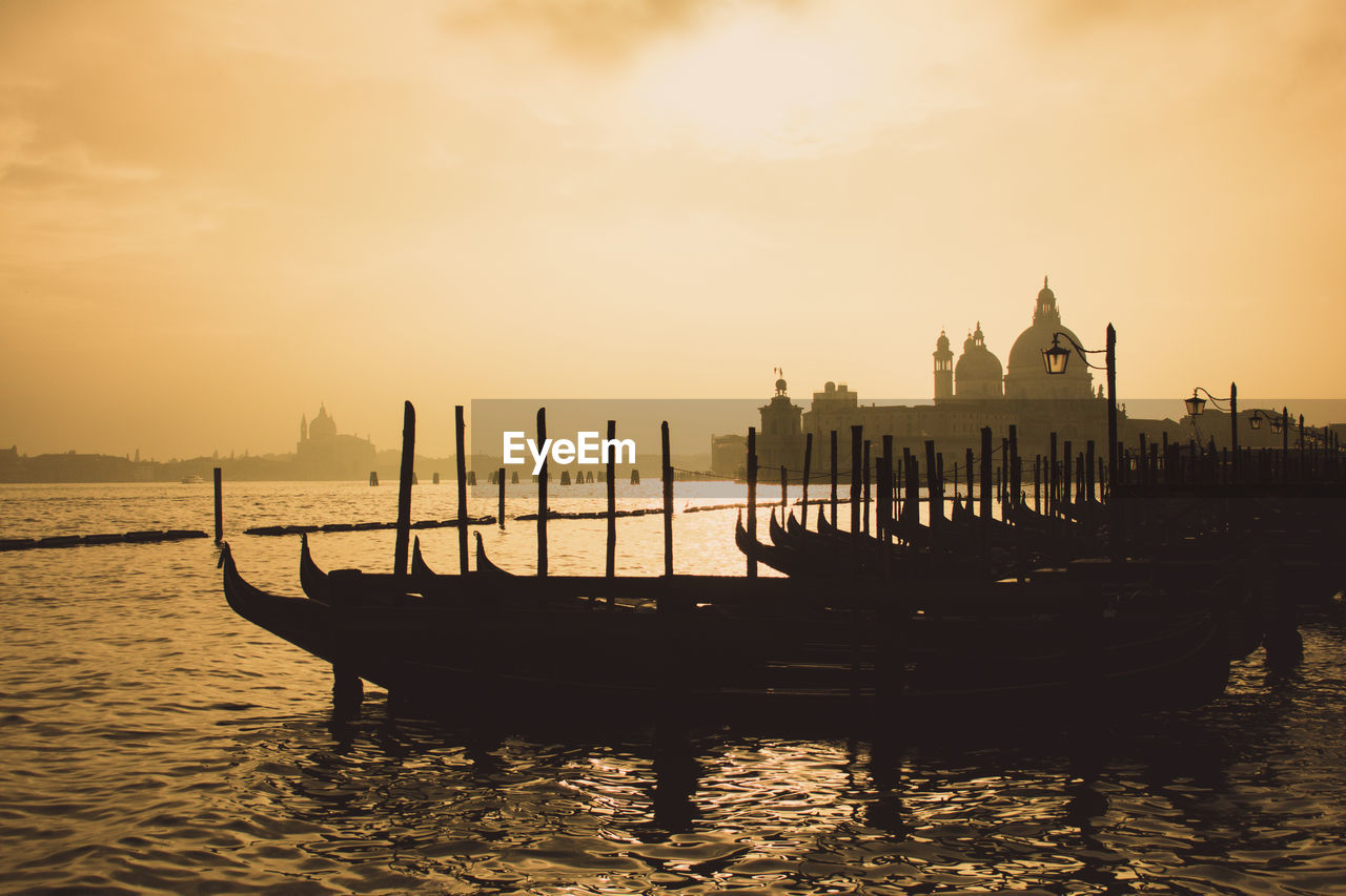 Boats moored in canal against sky during sunset