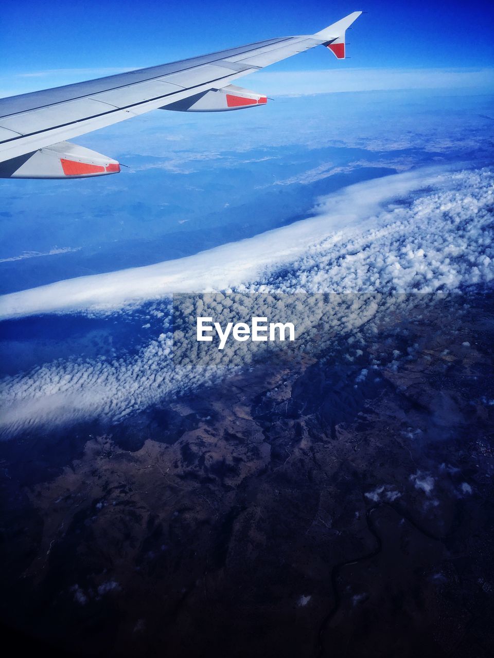 CROPPED IMAGE OF AIRPLANE WING OVER LANDSCAPE AGAINST SKY