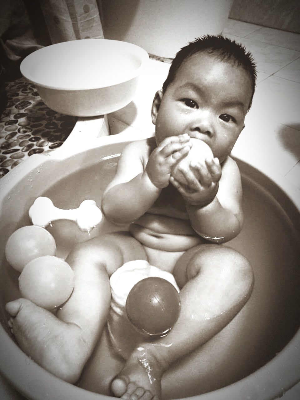 Portrait of toddler playing with balls while taking bath in bathtub