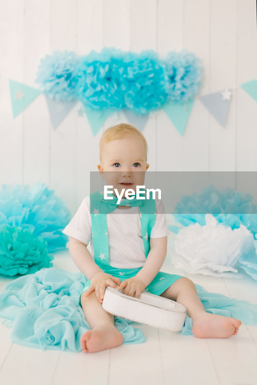 A one-year-old boy in a summer suit with a butterfly sits on the photo zone of his birthday 