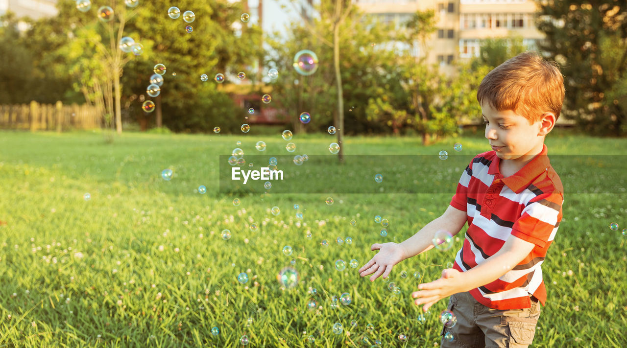 Smiling boy playing with bubbles while standing at park