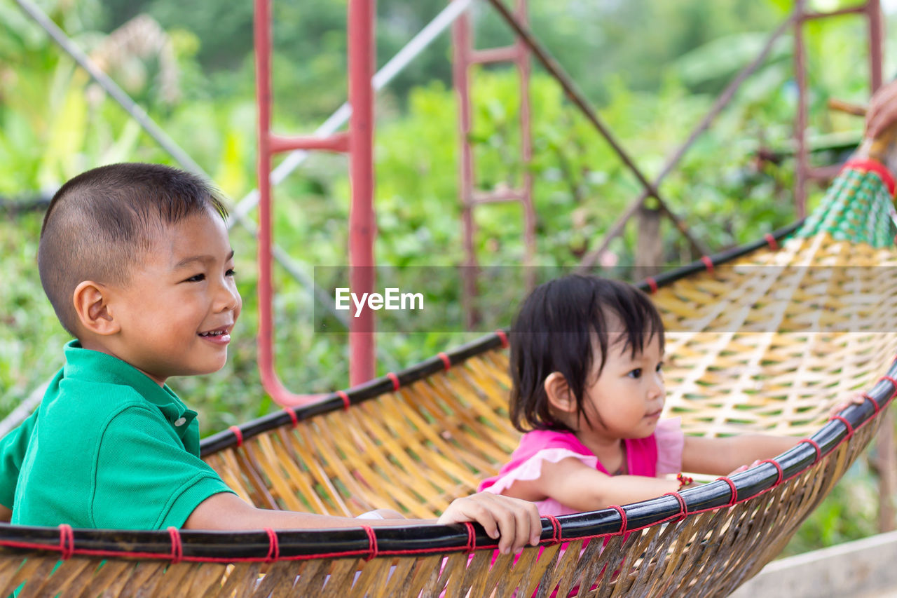 Male and female siblings sitting in hammock by farm