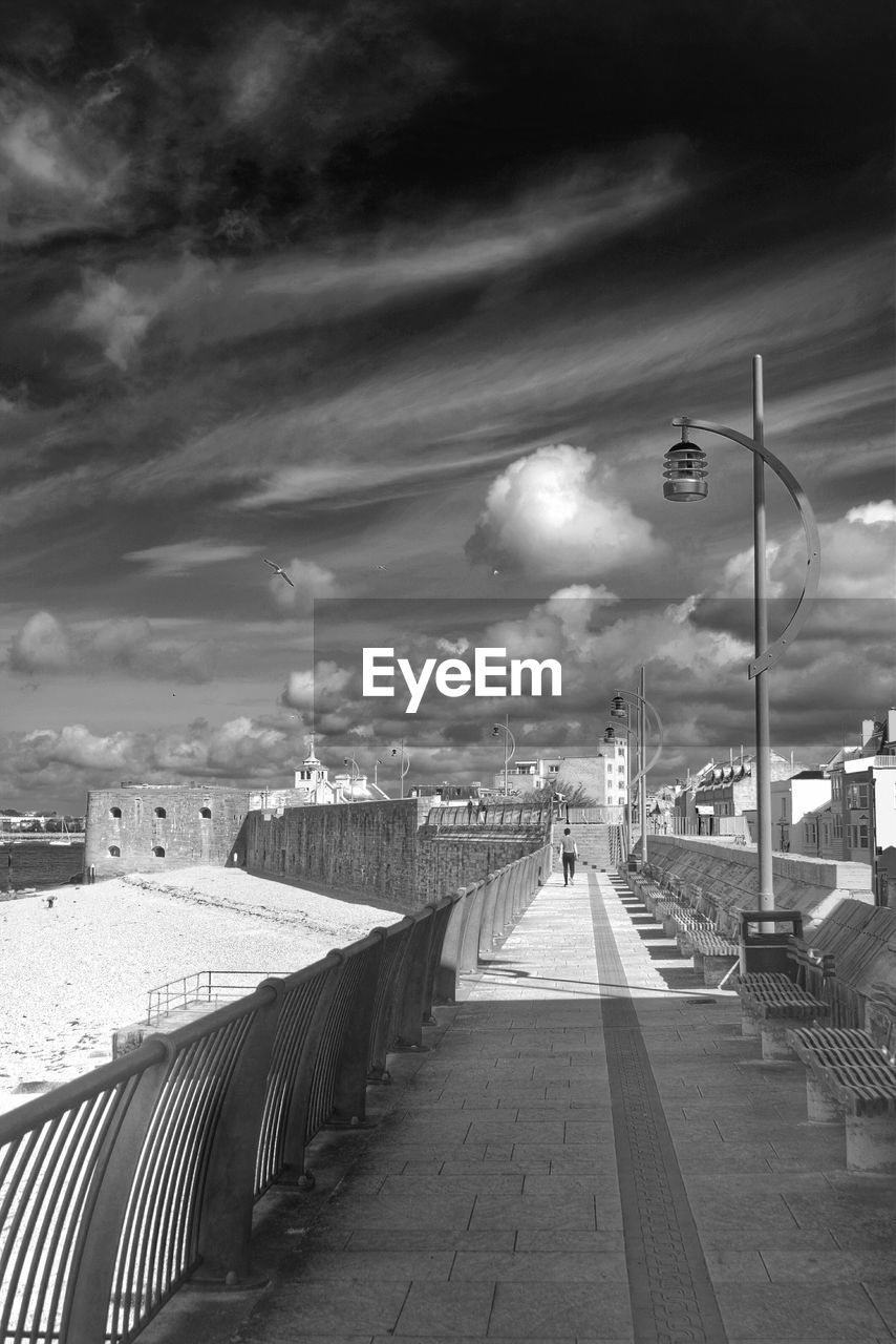 Full length rear view of man walking on footpath against cloudy sky