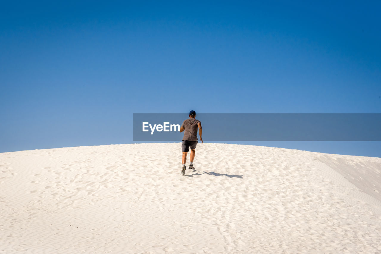 Rear view of man running on sand dune at desert