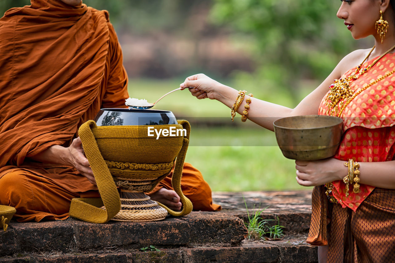 Young woman wearing traditional clothing taking cooked rice from container by monk