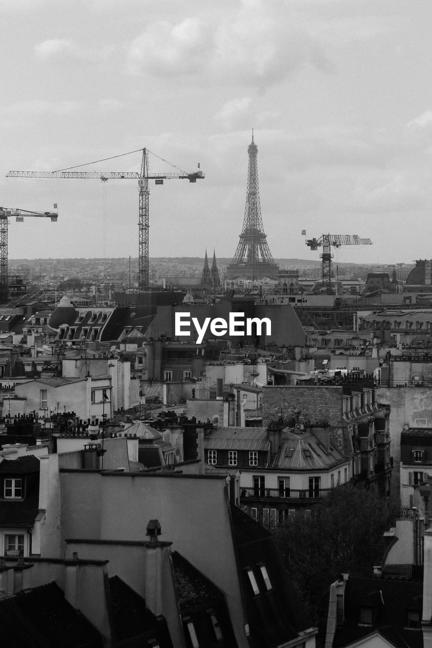 Eiffel tower and cranes in city against sky