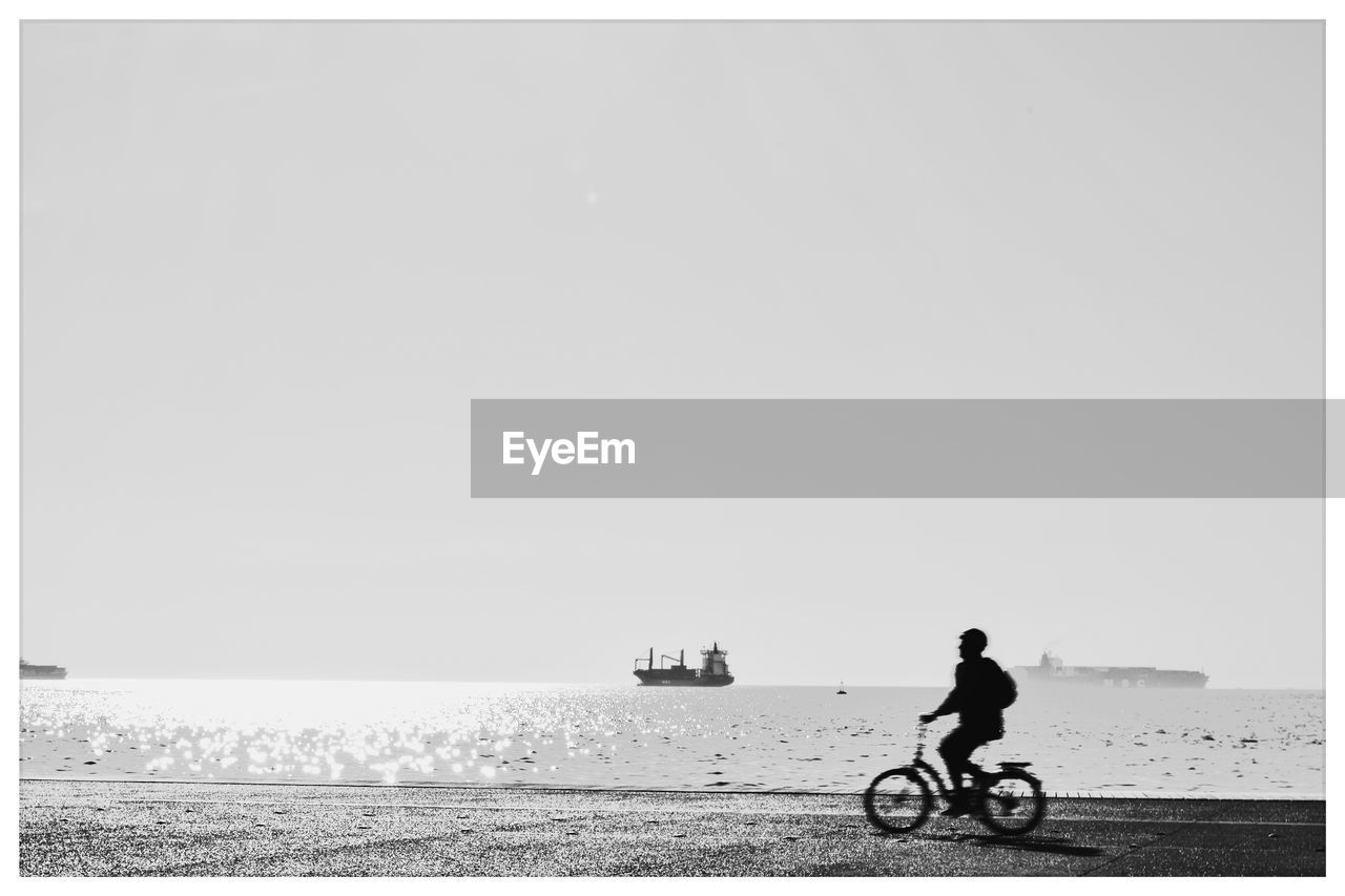 Silhouette man riding bicycle by sea against clear sky