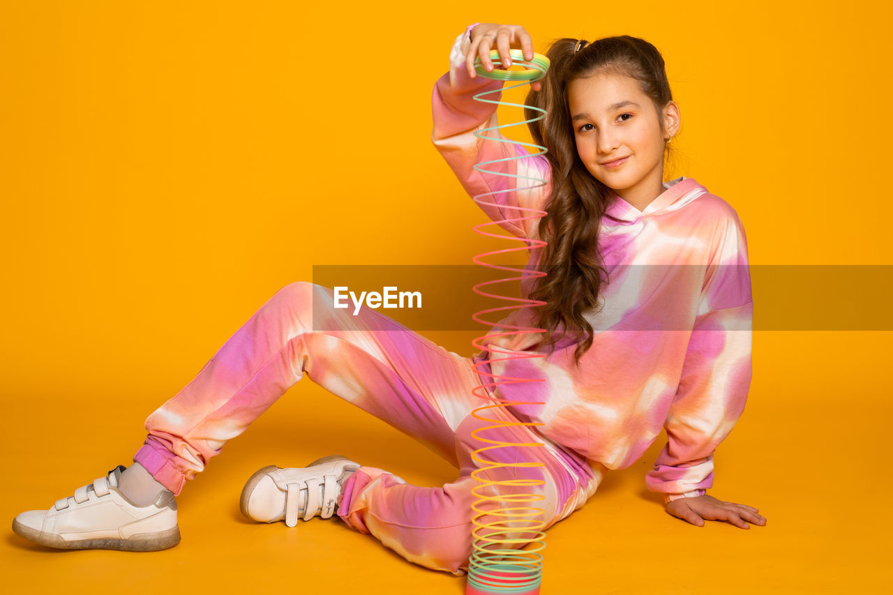 studio shot, colored background, women, portrait, one person, smiling, full length, indoors, yellow, yellow background, happiness, looking at camera, adult, sports, child, female, pink, person, young adult, lifestyles, emotion, childhood, clothing, modern dance, fashion, shoe, dancing, fun, hairstyle, cheerful, orange color, human face, footwear, exercising