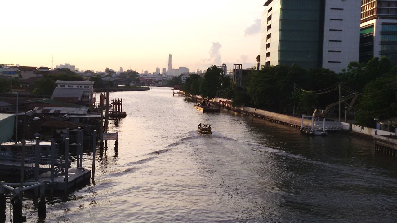 Ferry sailing in river by buildings in city against sky