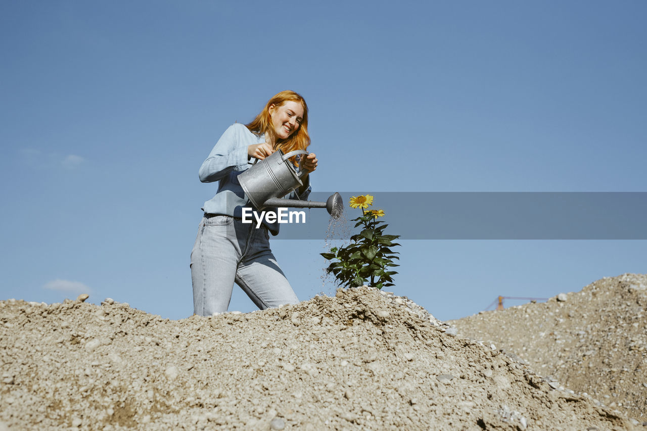 Smiling woman watering plant at construction site on sunny day