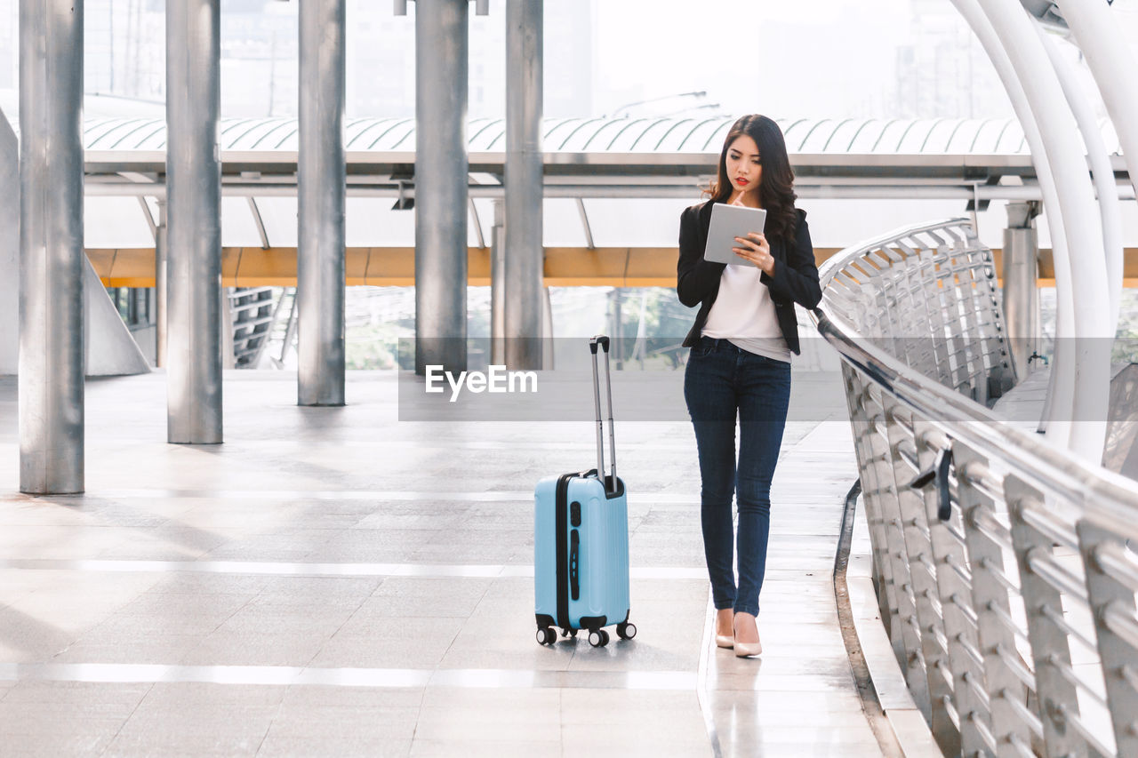 Businesswoman with luggage while using digital tablet 