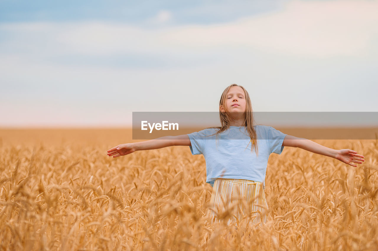 Girl with arms outstretched standing on wheat field
