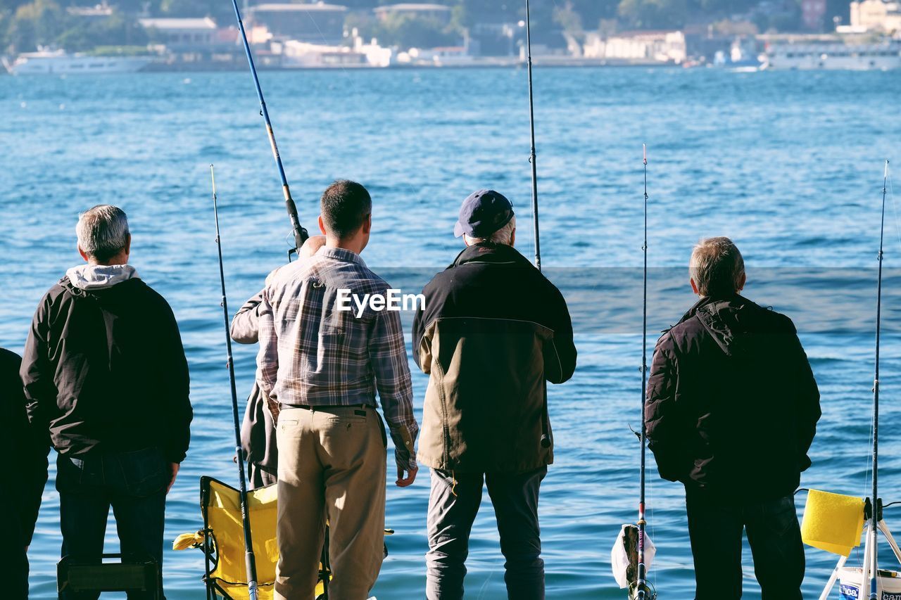 Rear view of fishermen fishing by river