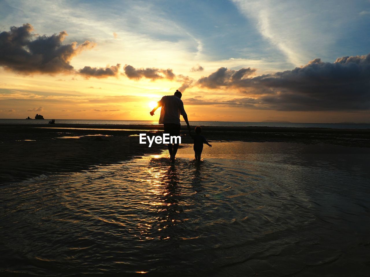 Silhouette of man with son standing on shore during sunset