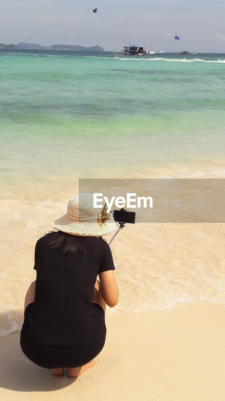 REAR VIEW OF WOMAN PHOTOGRAPHING SEA AGAINST THE SKY