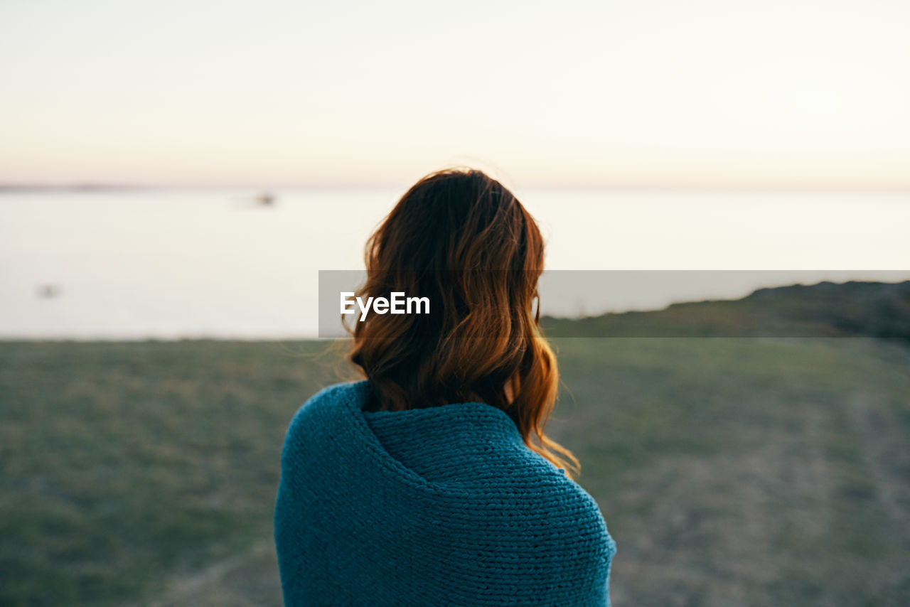 REAR VIEW OF WOMAN LOOKING AT SEA SHORE AGAINST SKY