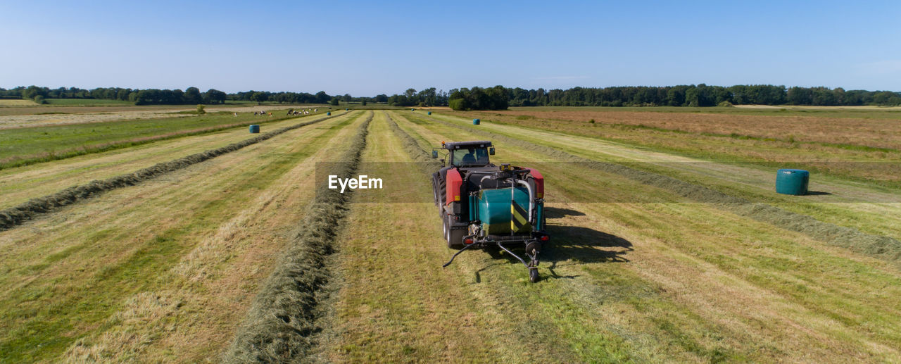 Black tractor with a red straw chamber press during the straw harvest on a mown field