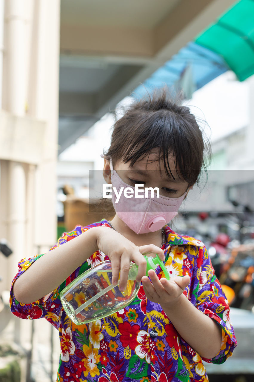 Cute girl wearing mask using hand sanitizer outdoors