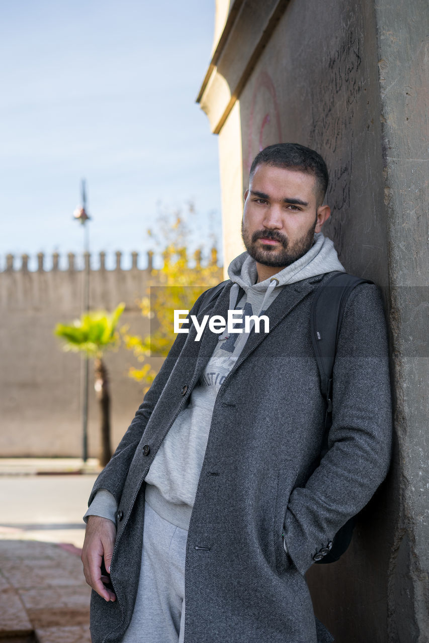 Moroccan man leaning against a wall wearing stylish grey coat