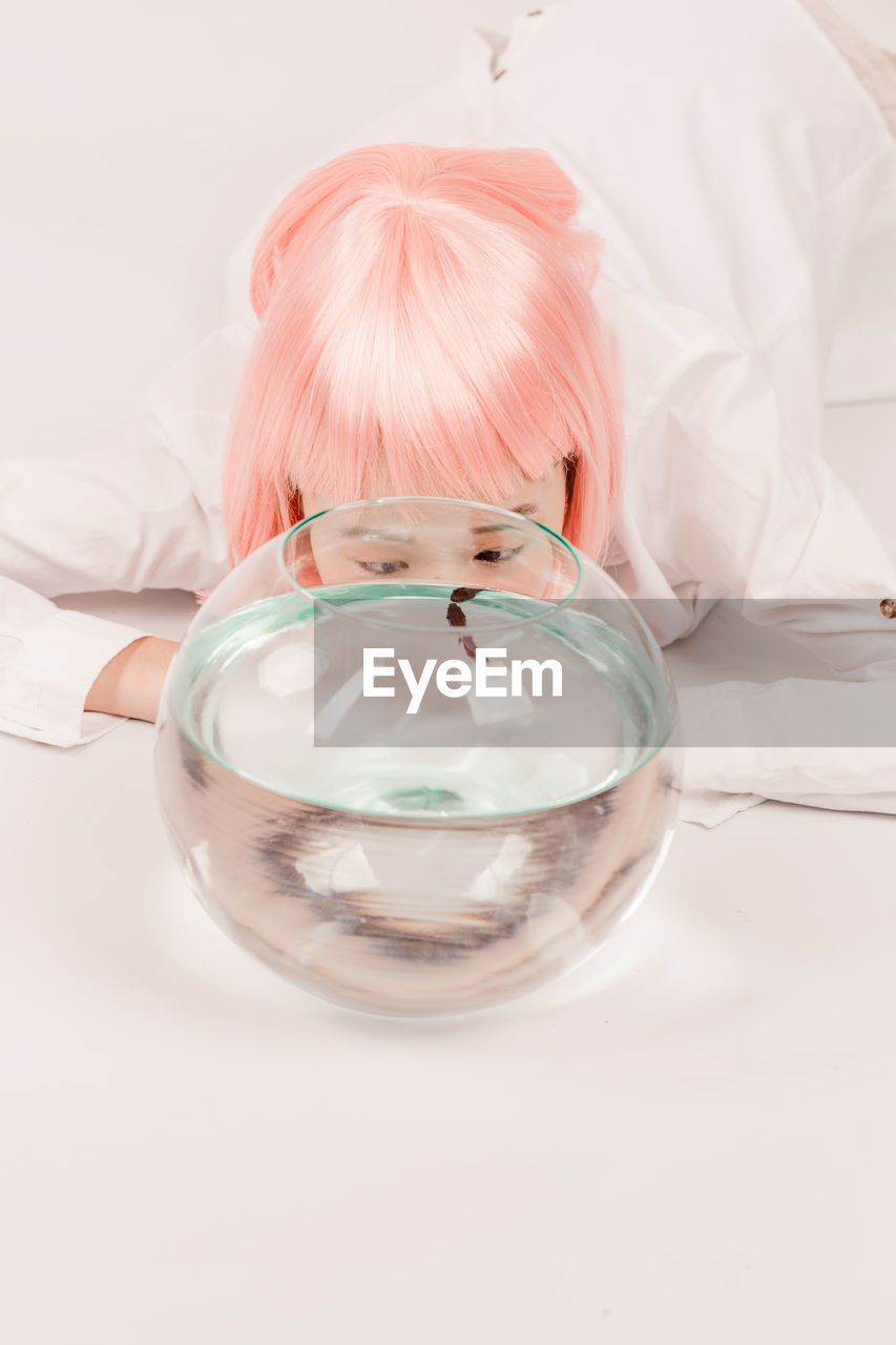 Close-up of woman by fish swimming in glass bowl on floor