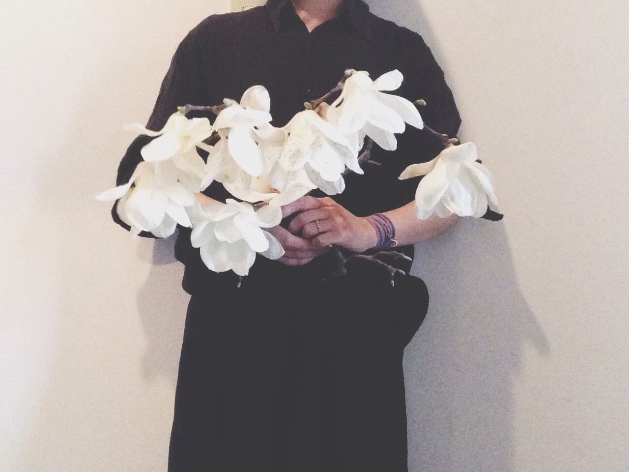 Midsection of woman holding white flowers against wall at home