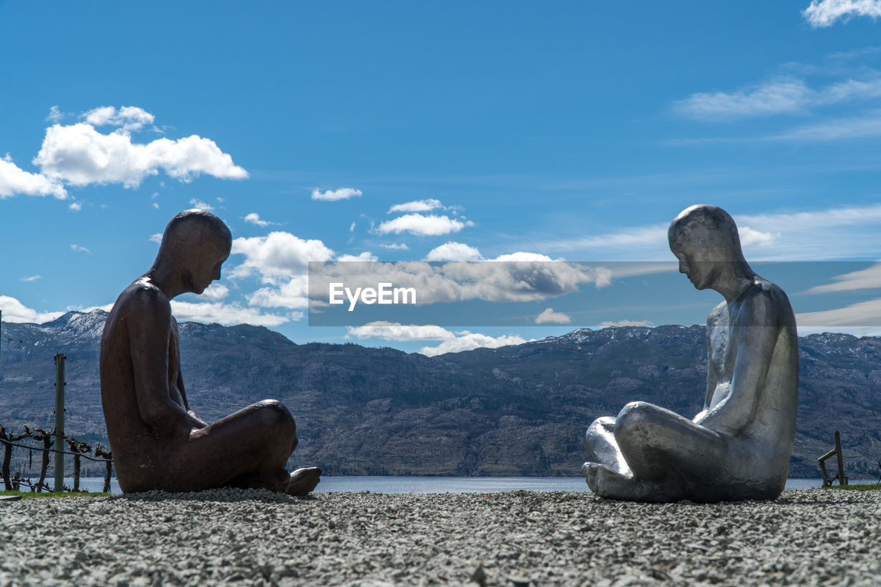 PEOPLE SITTING ON LAND AGAINST SKY