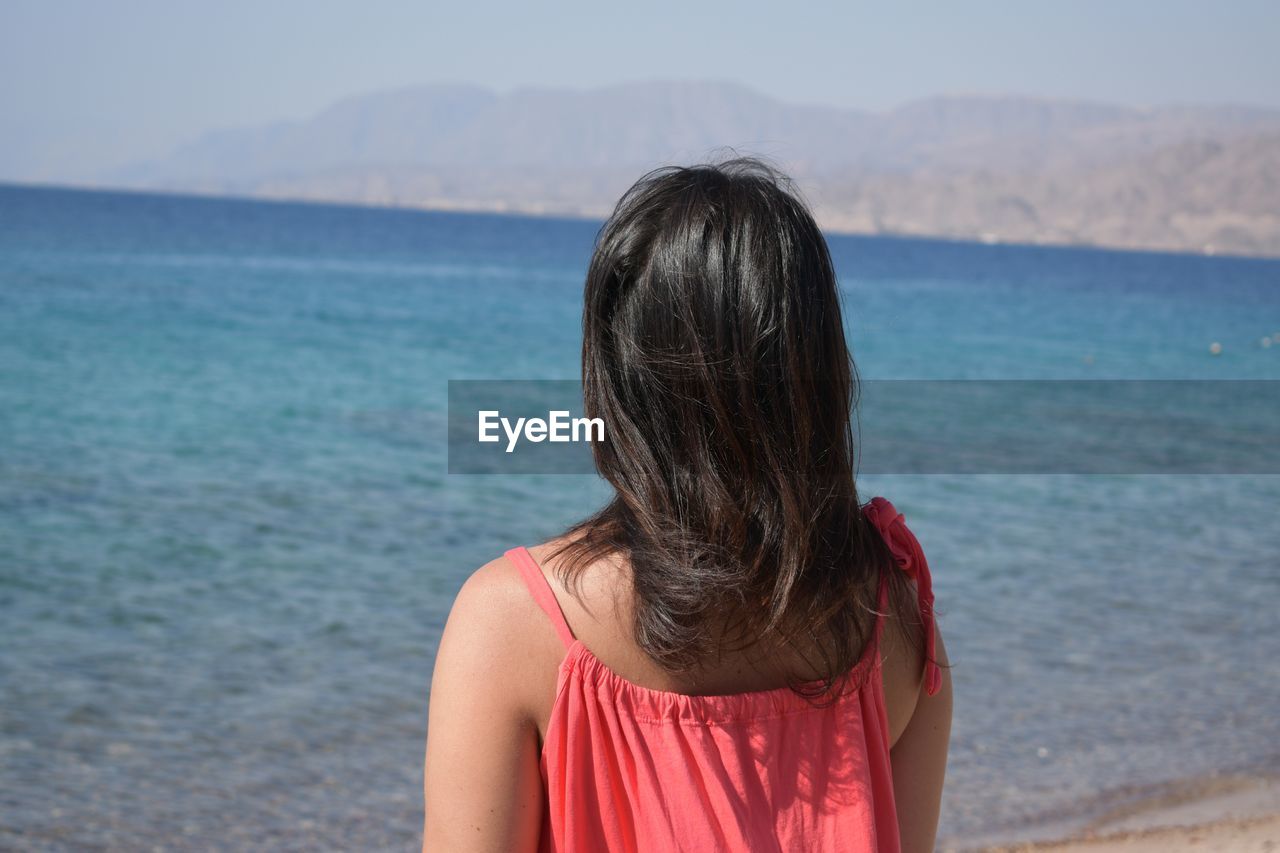 Rear view of woman standing at beach on sunny day