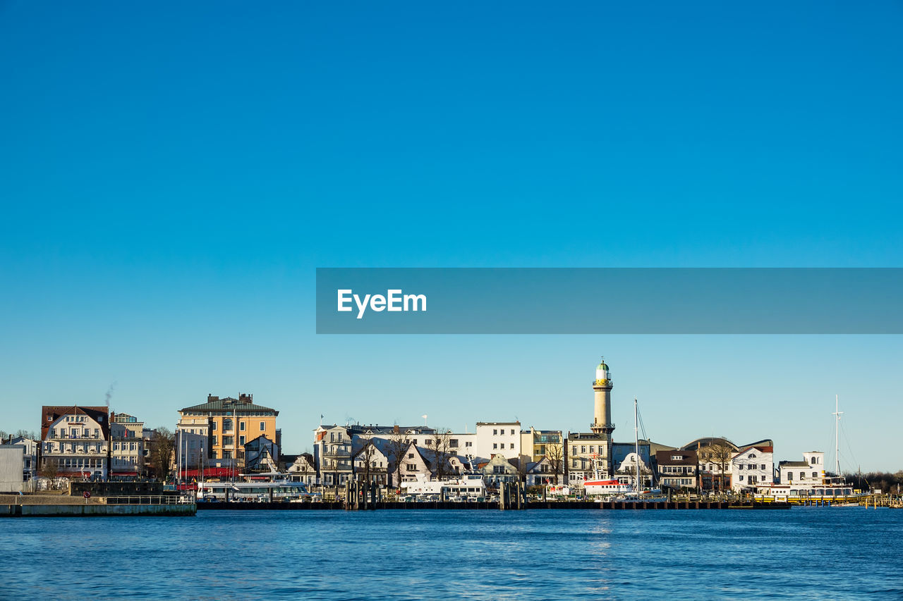 View of city at waterfront against blue sky