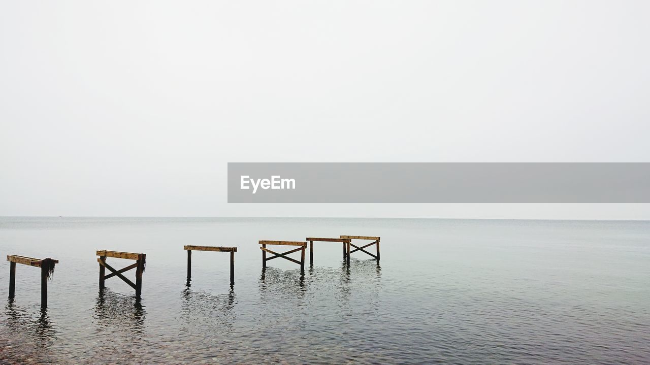 WOODEN POSTS ON SEA AGAINST CLEAR SKY