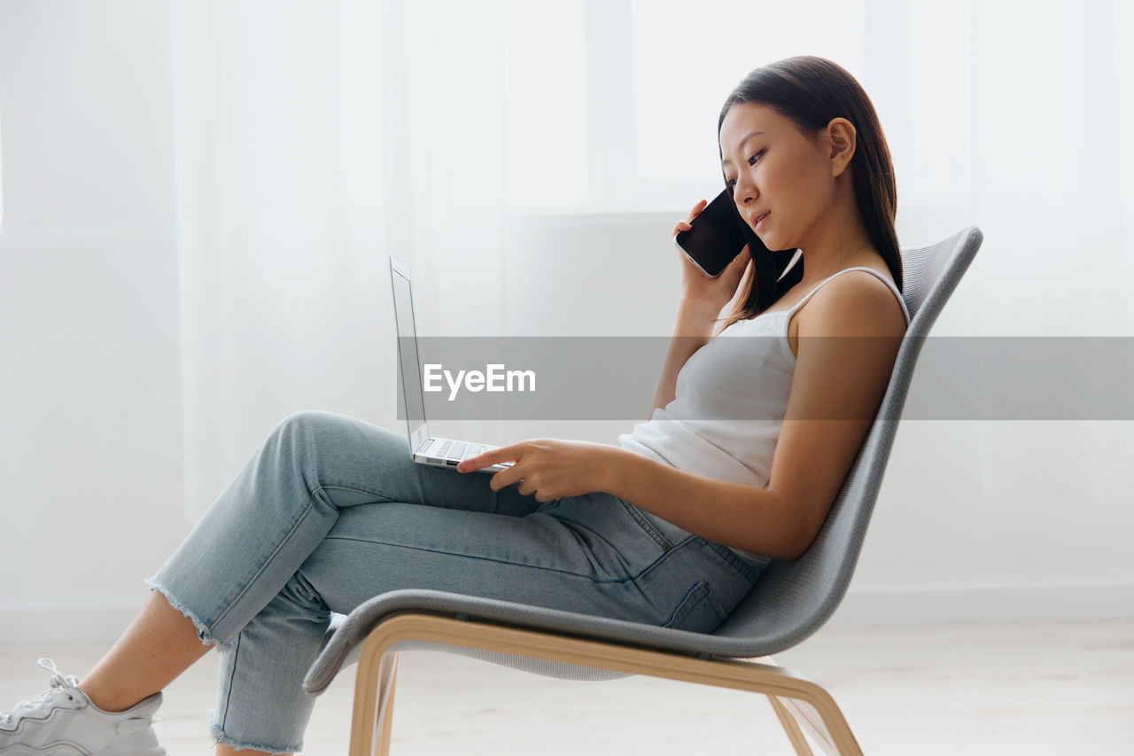 young woman using phone while sitting on sofa at home