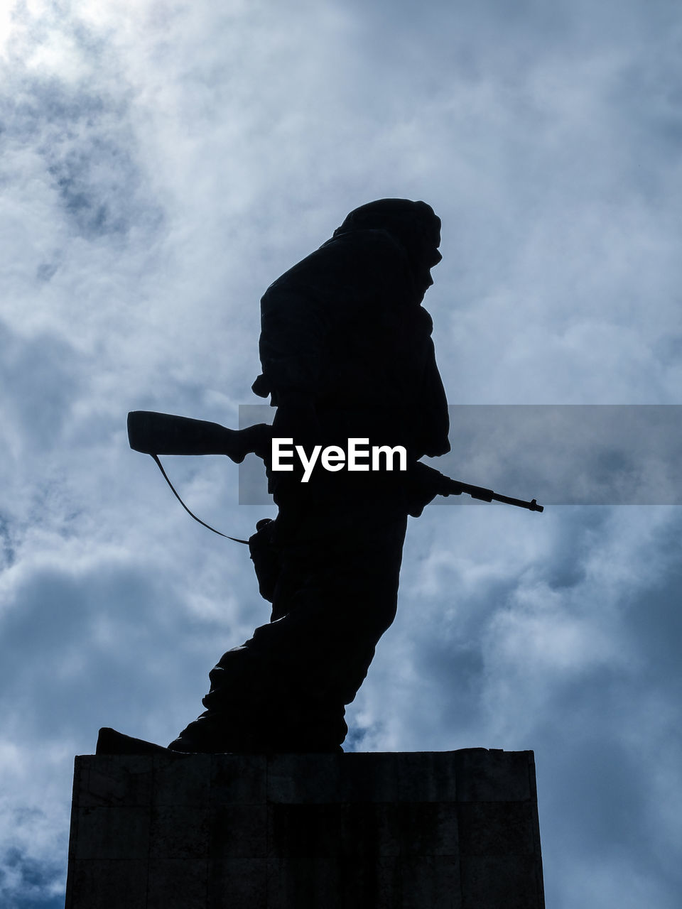 Low angle view of silhouette statue with gun against sky
