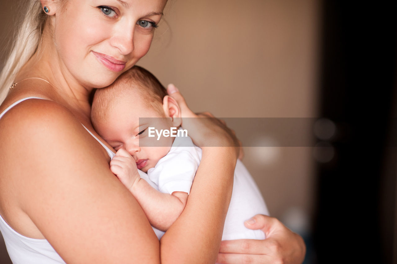 Smiling mother holding sleepy baby at home