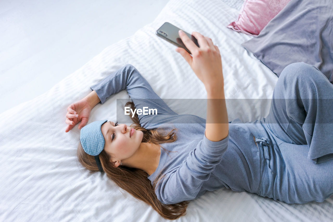 Beautiful woman in blue pajamas looking into phone. morning starts with phone.