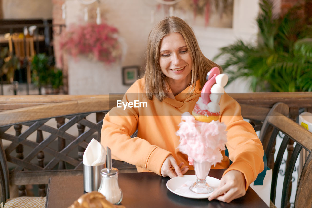 Happy woman eating sweet dessert in form pink flamingo in restaurant, woman