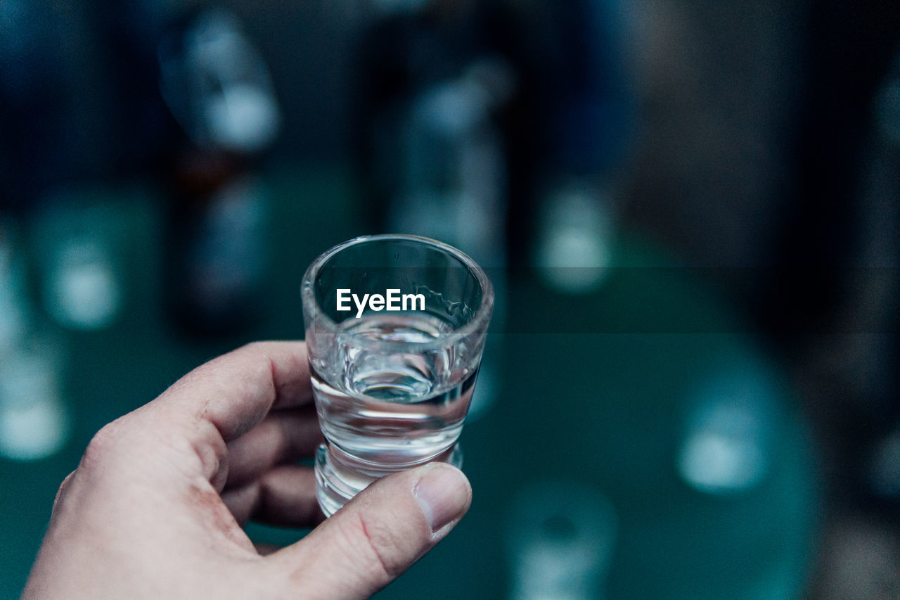 Close-up of hand holding glass against water