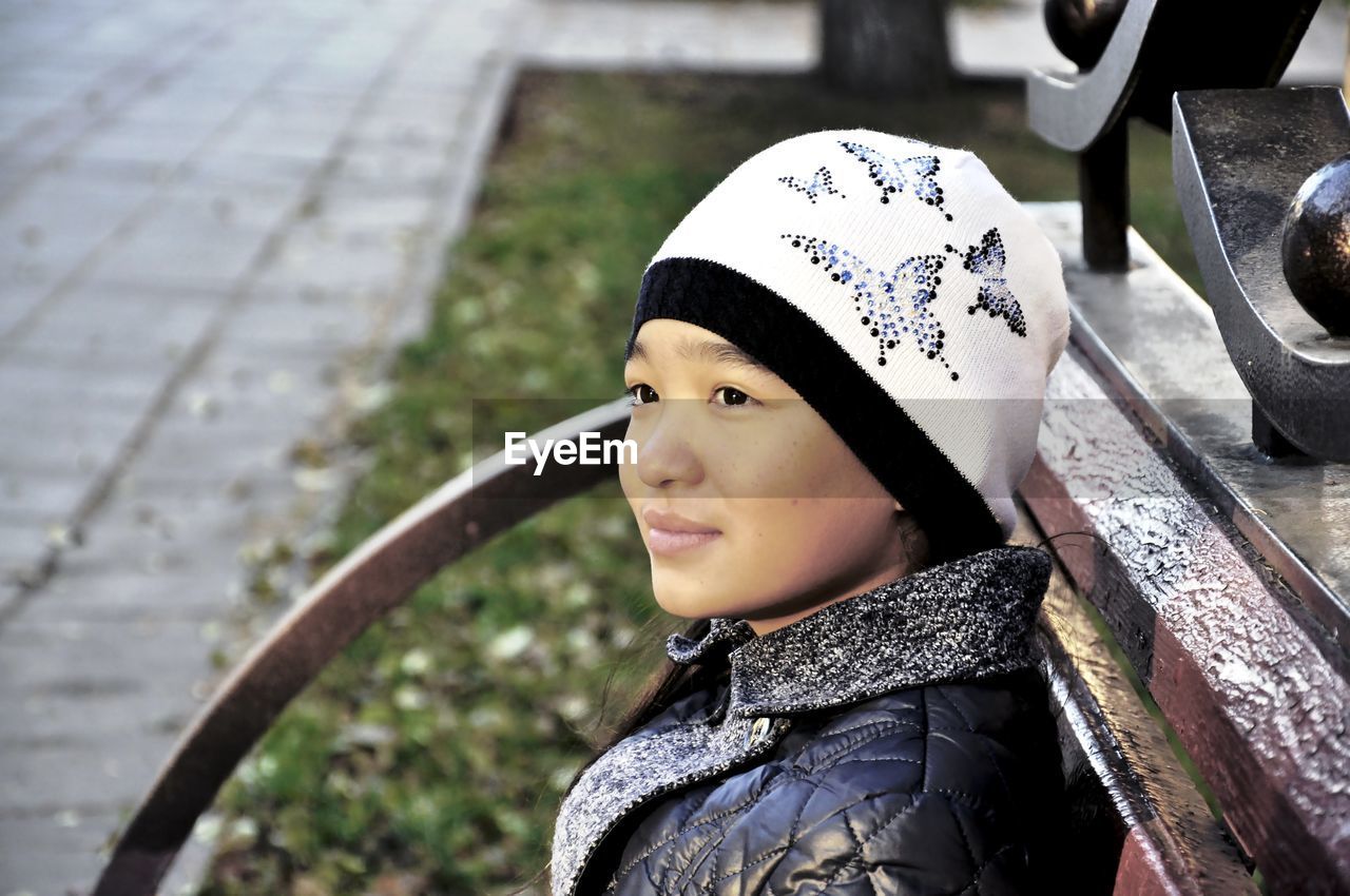 Thoughtful girl wearing knit hat while sitting on bench at park