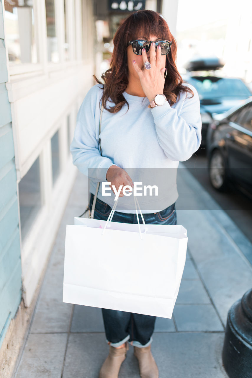 Full length of woman holding shopping bag on sidewalk