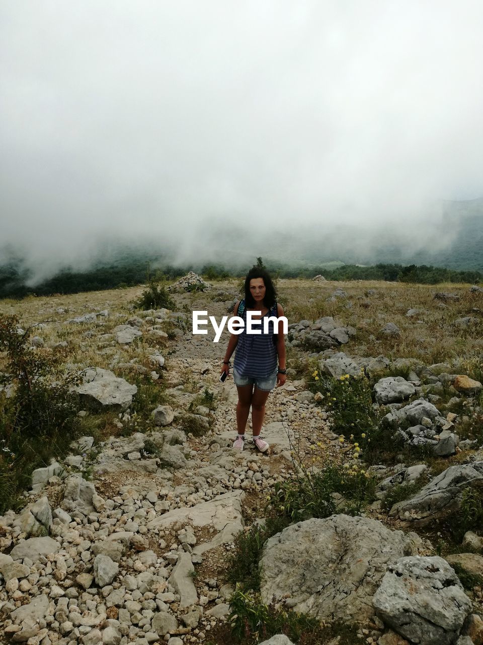 Full length of young woman standing on mountain during foggy weather