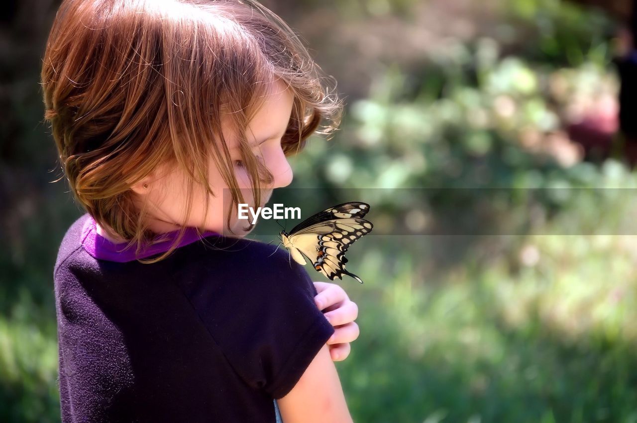 Rear view of girl looking at butterfly on shoulder