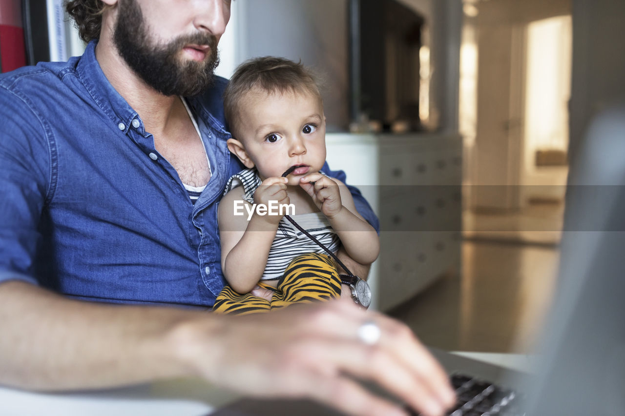 Portrait of baby boy with father using laptop at home