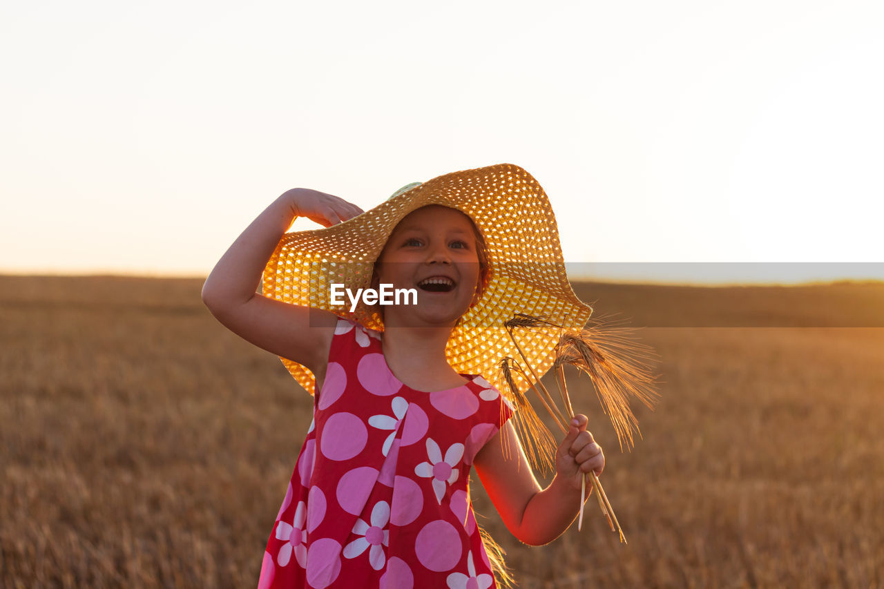 Adorable little girl in a straw hat pink summer dress in wheat field. child with long hair on sunset