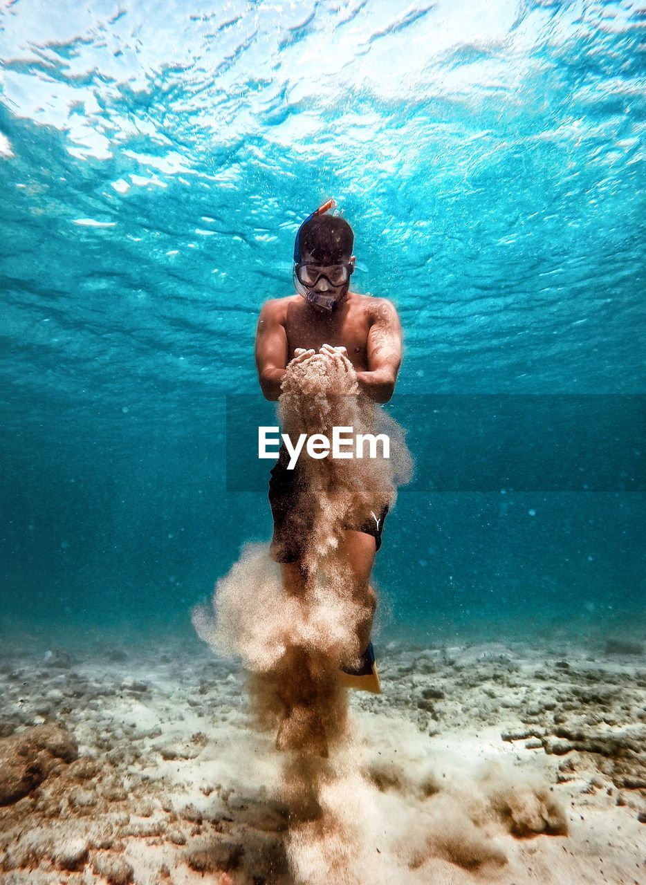 Shirtless man holding sand while swimming in sea