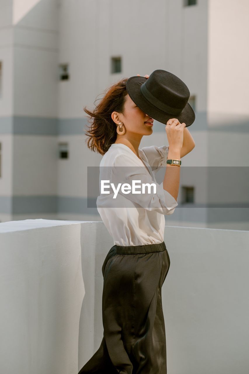 SIDE VIEW OF WOMAN WEARING HAT HOLDING CAMERA