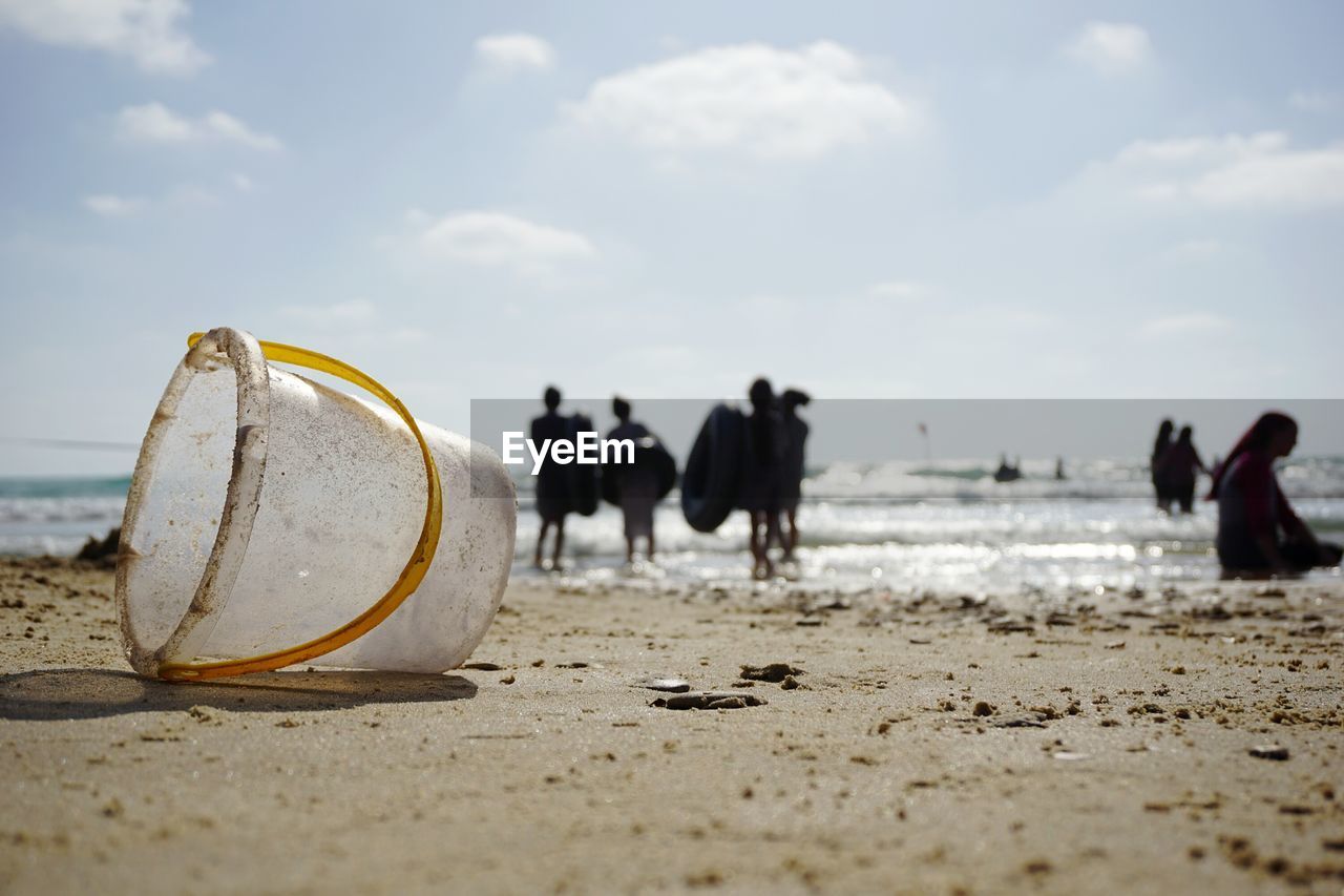 Bucket by people at beach against sky
